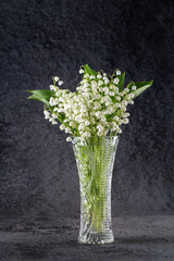 Bouquet of delicate lilies of the valley in a glass vase on a dark background