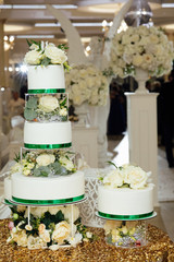 A large royal cake in white color decorated with many flowers and roses at a luxury wedding with a very beautiful decor. Dessert for festive dinner of the bride and groom.