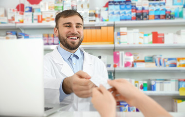 Naklejka na ściany i meble Professional pharmacist giving pills to customer in modern drugstore