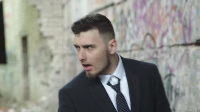 Man in suit corrects necktie, looks around and flees at ruins