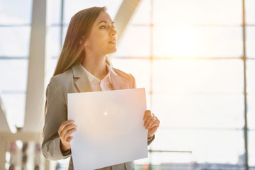 Portrait of businesswoman standing while holding blank white board in arrival area at airport