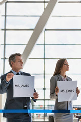 Business people waiting while holding white placard with their boss name in arrival area at airport