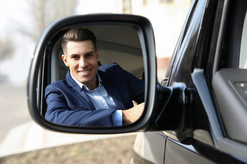 Handsome man looking into side view mirror of modern car outdoors