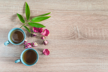 Obraz na płótnie Canvas Tea time composition. Two cups of tea, red rose buds and green bamboo leaves on wooden background. Space for text, top view