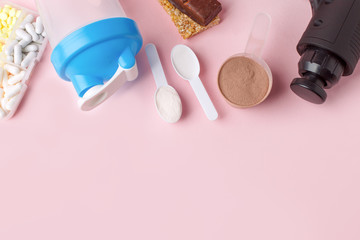 Therapeutic percussive massage gun, fit meal, pills, sport energy bar on pink background - concept of modern sport activity and diet, health lifestyle routine, wellness, healthcare, copy space