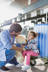 Obraz premium Portrait of man holding teddy bear and playing with his daughter in check in area at airport