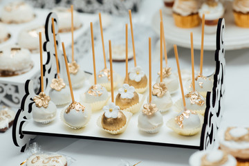 Modern sweet table at celebration. Stylish candy bar with delicious cakes, cookies, cupcakes in gold and white colors. Luxury catering in restaurant. Wedding reception.