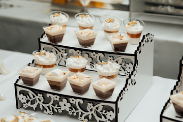 Modern sweet table at celebration. Stylish candy bar with delicious cakes, cookies, cupcakes in gold and white colors. Luxury catering in restaurant. Wedding reception.