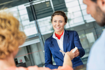 Portrait of young attractive passenger service agent giving boarding with passenger after check in at airport - obrazy, fototapety, plakaty