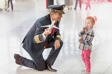 Portrait of mature pilot holding airplane toy while playing with cute little girl in airport