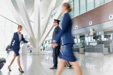 Mature pilot with young beautiful flight attendants walking in airport