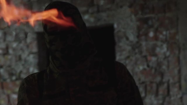 Man in camouflage uniform starts a fire and looks dowm in catacomb