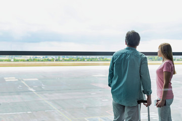 Fototapeta premium Rear view of mature man looking through the window with his daughter in airport