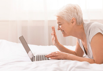 Cheerful grandmother talking with relatives via laptop online