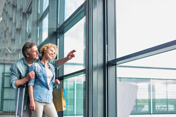 Mature man hugging his wife from behind while looking through the window in airport