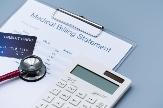 top view picture of medical billing statement, cradit card, white calculator and pink stethoscope on the gray background