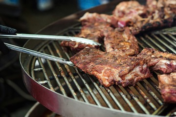 Street festival. Barbeque, BBQ concept. Cooking grilled pork ribs. Food catering, party. Chef with tongs holding hot pork ribs.