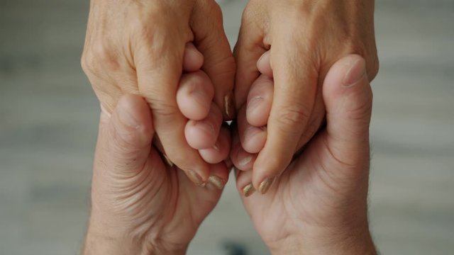 Close-up of happy senior couple holding hands, man is caressing woman's palms expressing tenderness, love and care. Feelings, emotions and people concept.