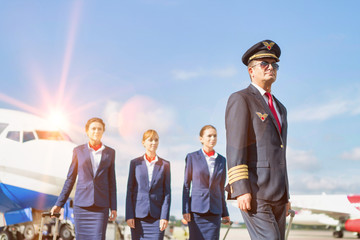 Portrait of mature pilot walking with three young beautiful flight attendants against airplane in...