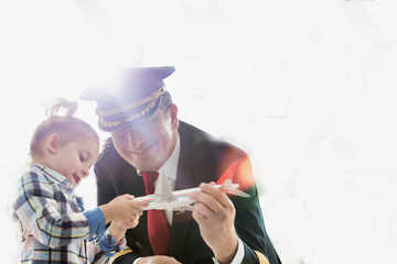 Portrait of mature pilot holding airplane toy while playing with cute little girl in airport