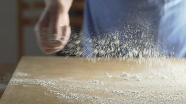 Amazing backlit close up shot of woman chef cook baker preparing bread or pizza, throwing flour on a wooden board in slow motion. Food concept. 
