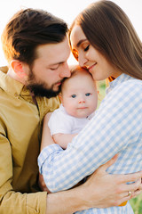 portrait of a happy young family, where mom and dad hug each other, holding their little child between them in the rays of the sunset, summer sun