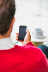 Rear view of businessman using smartphone while sitting and drinking coffee in lobby