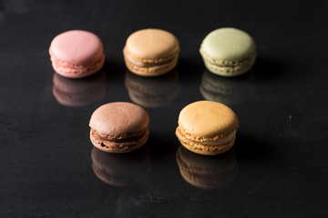 colored macarons on a black surface and with a reflection