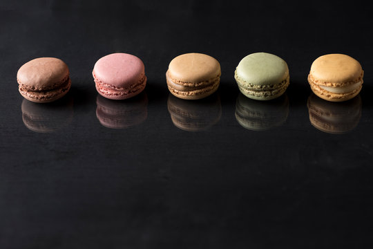colored macarons on a black surface and with a reflection