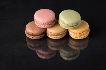 colored macarons on a black surface and with a reflection