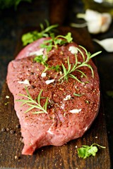 Fresh raw piece of beef steak with herbs and spices on wooden board on a dark background. A good piece of meat for cooking dinner.