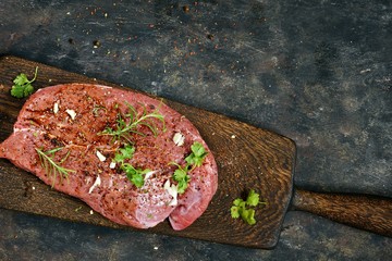 Fresh raw piece of beef steak with herbs and spices on wooden board on a dark background. A good...