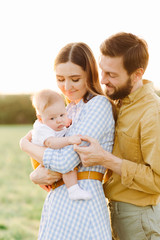 portrait of a happy young family, where mom and dad hug each other, holding their little child between them in the rays of the sunset, summer sun