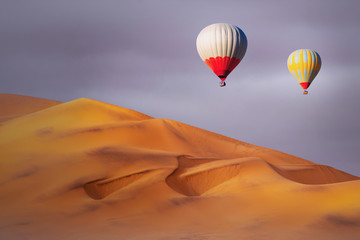 Colored hot air balloons flying over the sand dunes at sunset