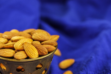 A metal bowl filled with almonds on a blue background