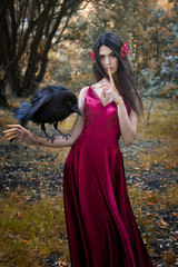 Art photo of a fairy-tale girl in the autumn forest with a big black raven on her hand