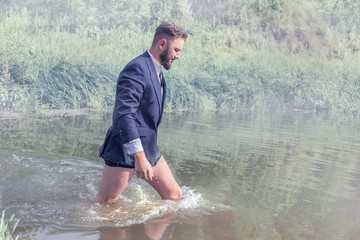 A man in a jacket, in a tie and without pants is walking through the swamp. Tired of the work of a man and he leaves.