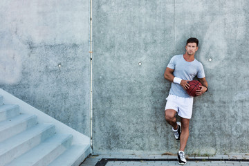 Young attractive man leaning on wall while holding ball