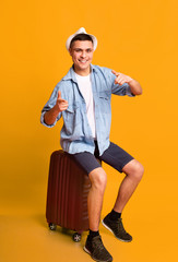 Traveler young man indicating at camera, sitting on luggage