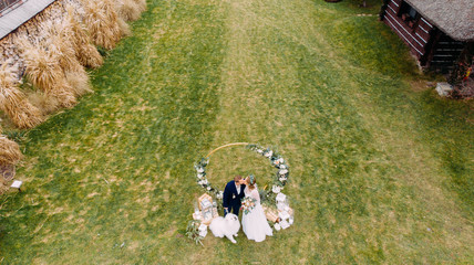 View from drone of the newlyweds kissing next to dog on the background of wedding arch.