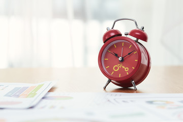 Close up of red clock on wooden table with many report paper near window with copy space