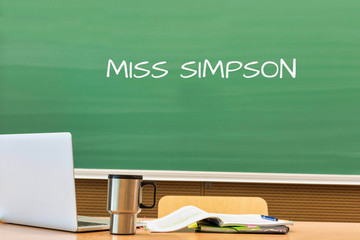 Teacher writing MISS SIMPSON on a green chalk board in her office