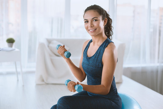 Charming young woman with dumbbells and gym ball on her workout indoors, empty space