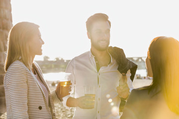 Business people celebrating success while drinking beer on the beach with lens flare in background