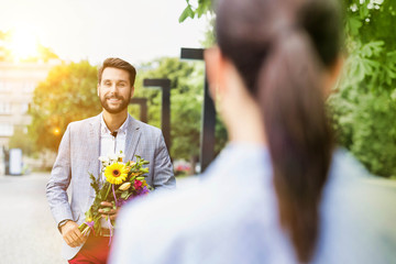 Portrait of young attractive man holding boquet of flowers for his girlfriend in park
