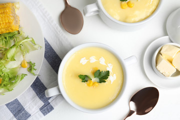 Delicious corn cream soup served on white table, flat lay