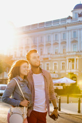 Portrait of young attractive couple walking in the middle of the city with lens flare in background