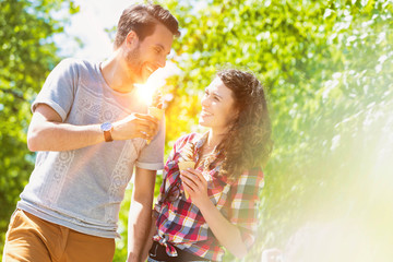 Fototapeta premium Portrait of young attractive couple walking while eating ice cream with lens flare in background