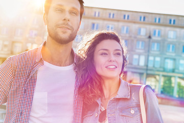 Portrait of young attractive couple standing against museum with lens flare in background