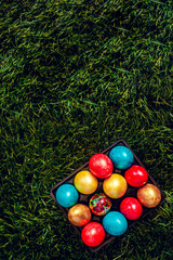 An egg carton full of colorful Easter eggs on the green grass background. View from above. Copy space for your text or ad